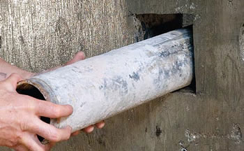 Metal pipe being inserted into a square hole cut into a concrete wall